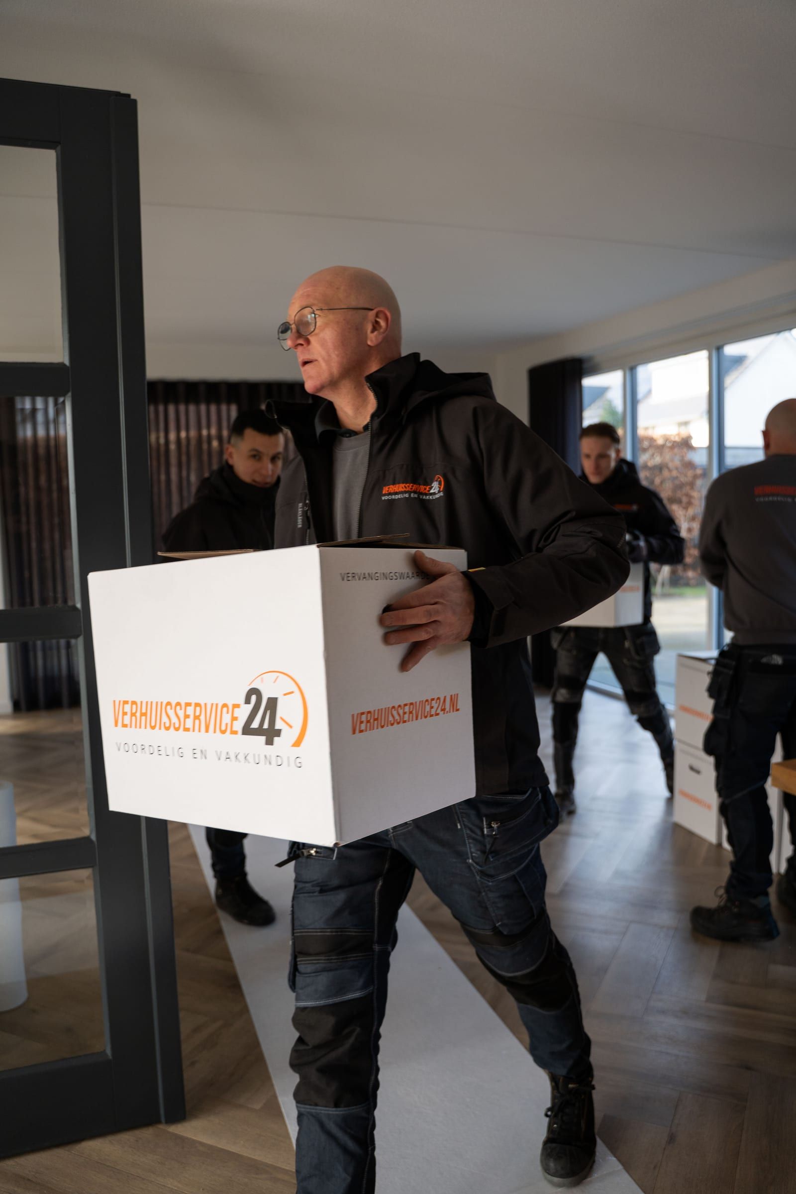 Verhuizer van Verhuisservice24 draagt een verhuisdoos door een woning met vloerbescherming