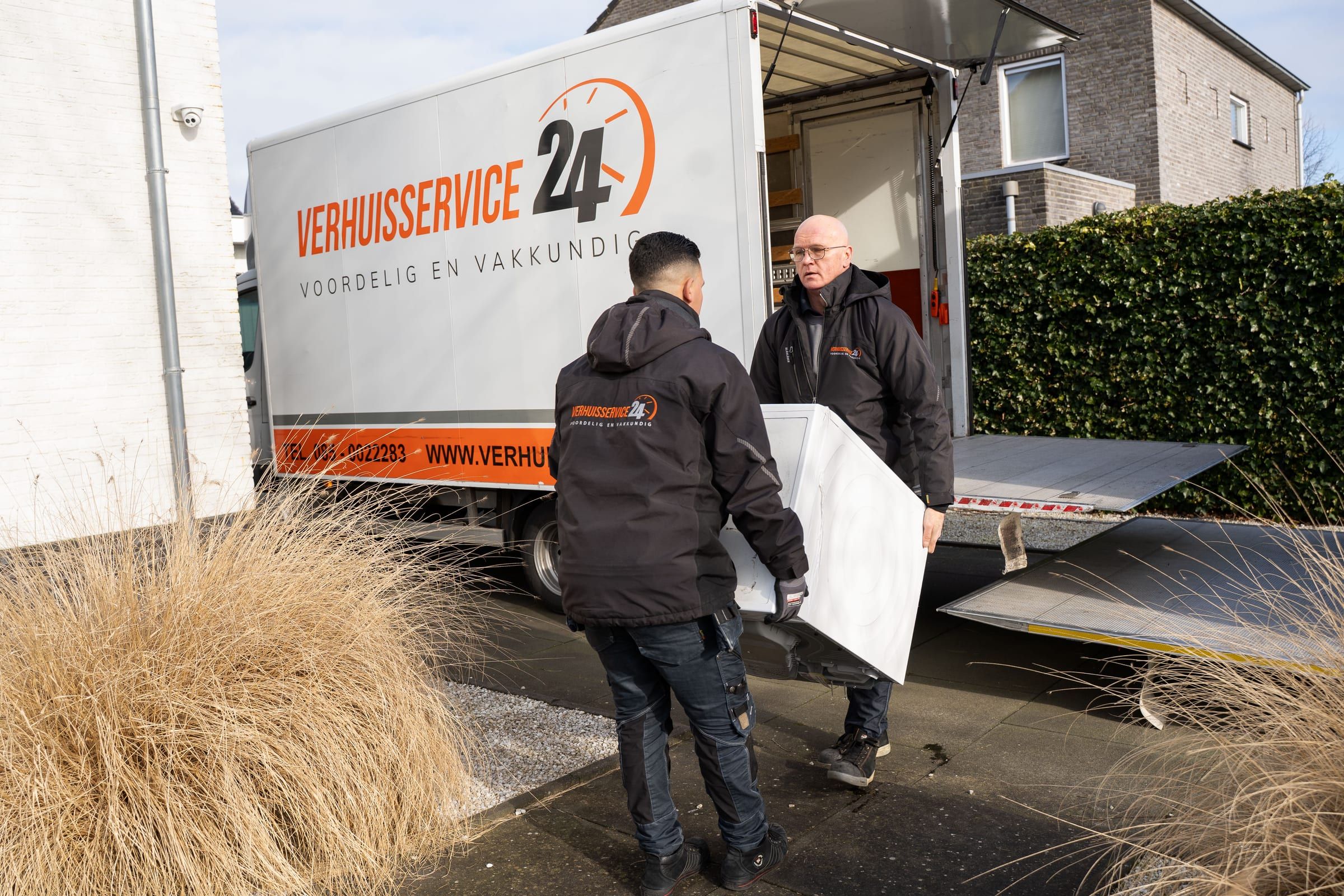 Twee verhuizers tillen een wasmachine van de laadklep van de verhuiswagen