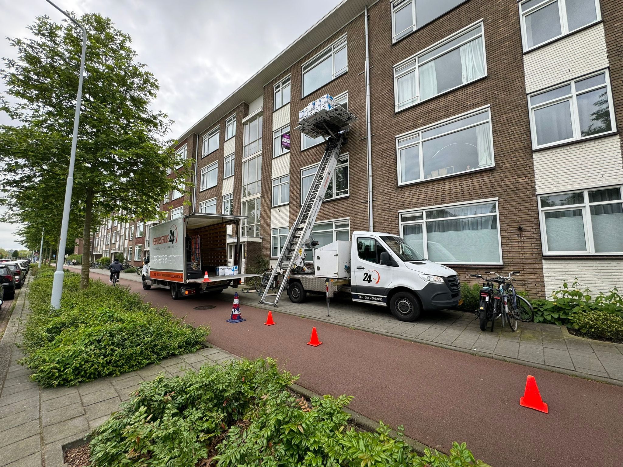 Verhuislift van Verhuisservice24 tegen een flat, met de verhuiswagen ervoor